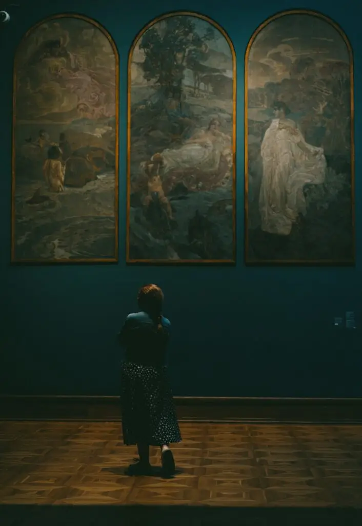 A girl looking up at three arched paintings in a gallery