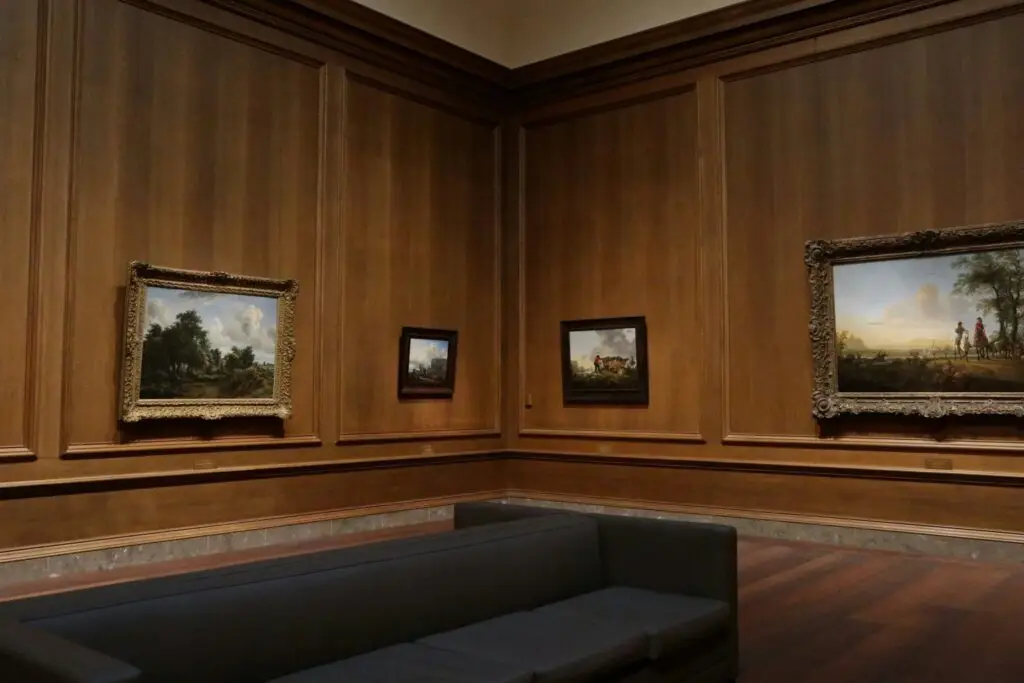 Landscape paintings in a wood-panelled gallery with a sofa