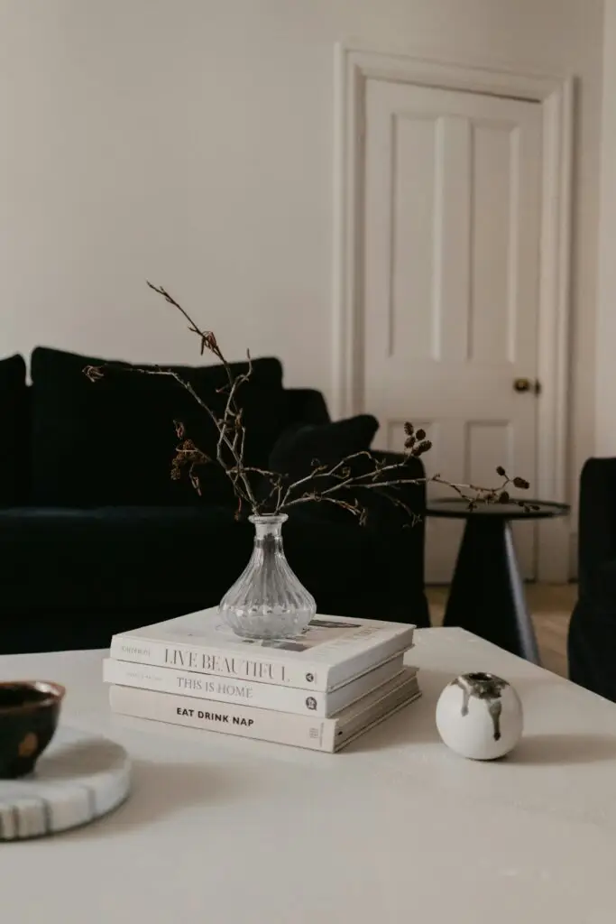 Coffee table books stacked beneath a glass vase of branches