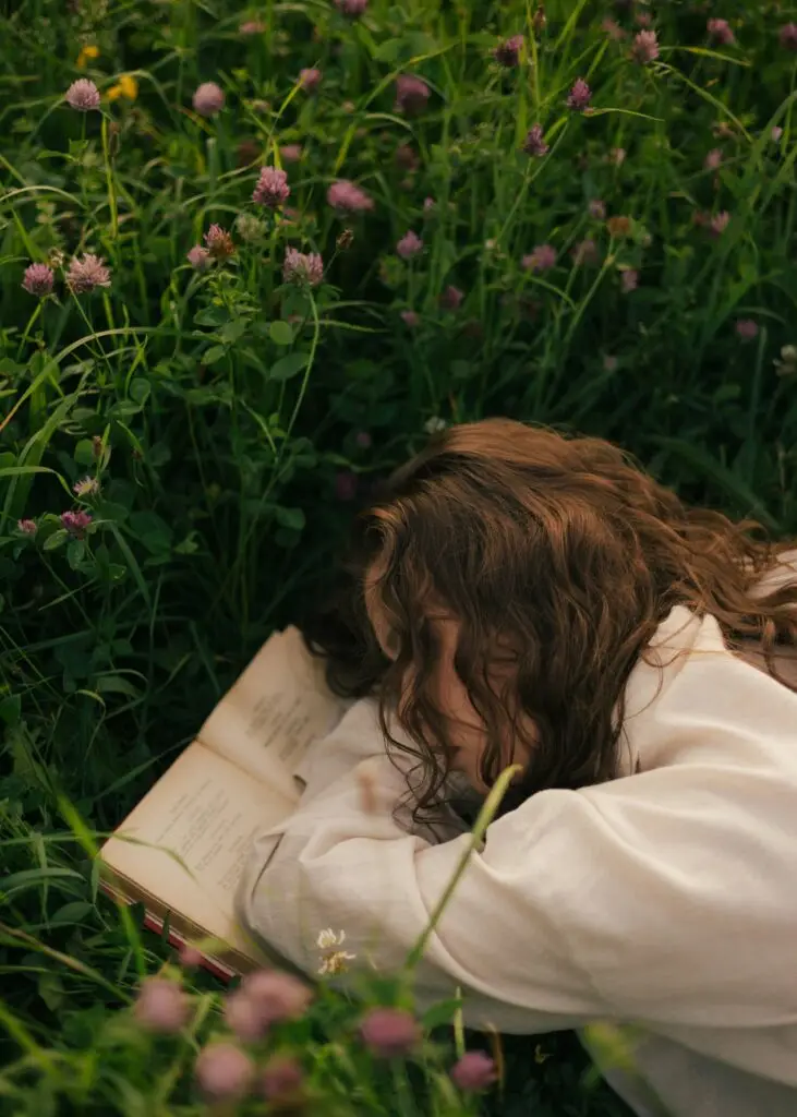 Woman resting her head on an open book in a meadow of clover