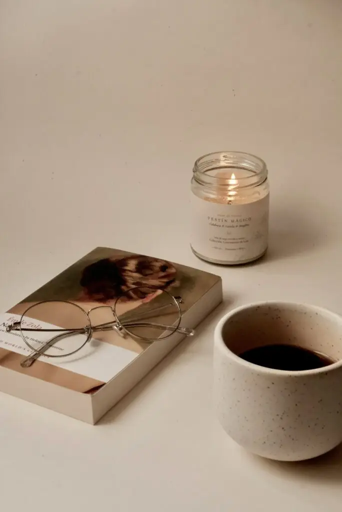 A lit candle, a book with reading glasses and a cup of coffee