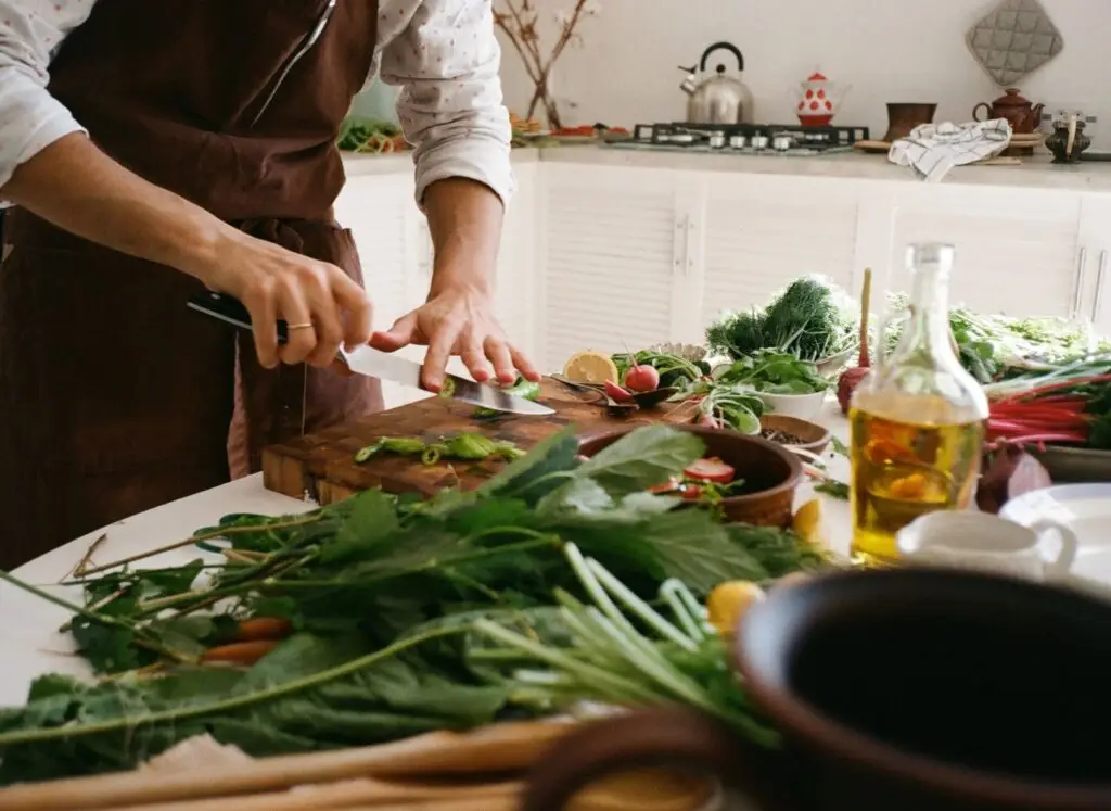 Hands chopping fresh greens in a home kitchen beside a bottle of olive oil