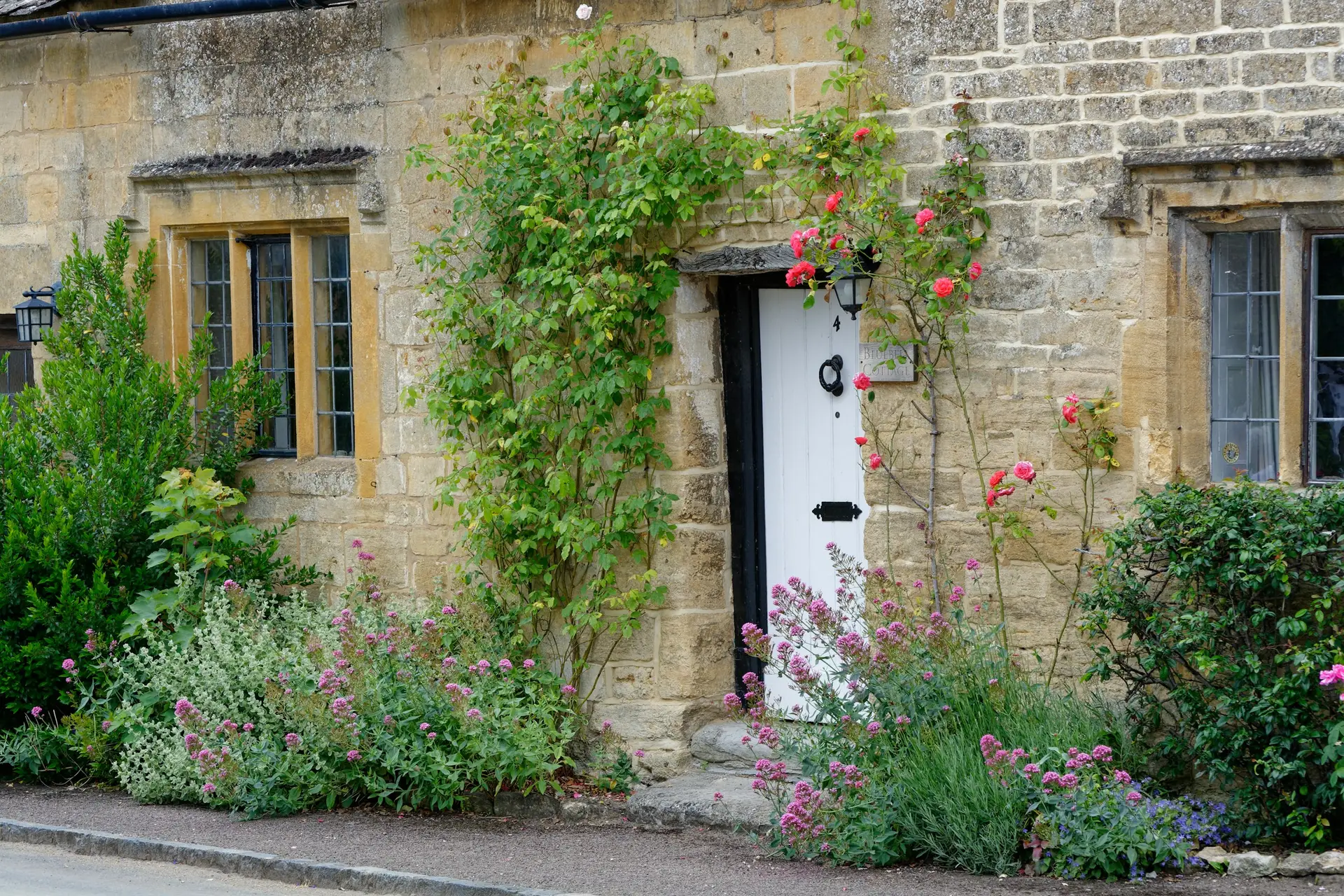 A Cotswold stone house with roses and a cottage garden by the door