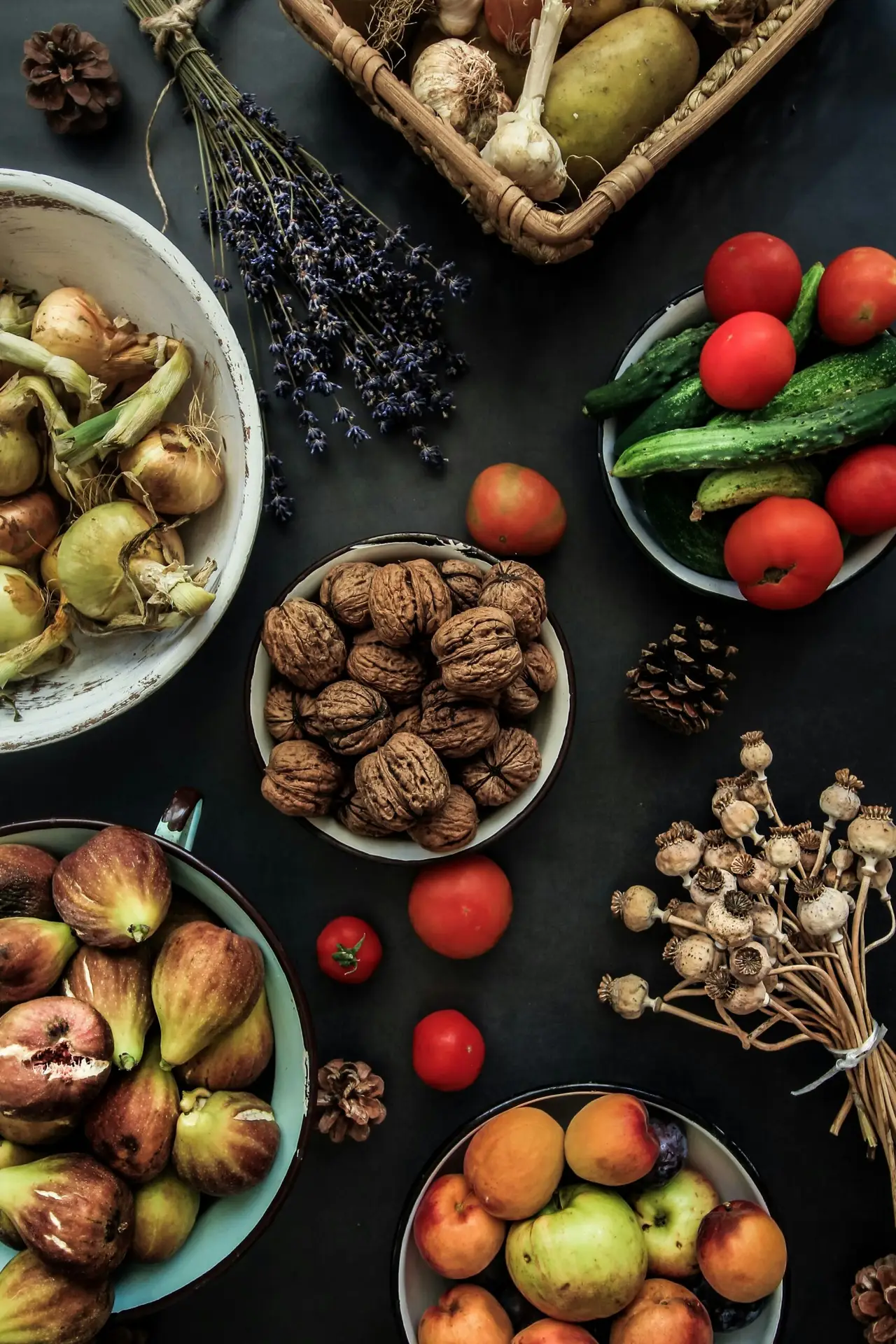 A bowl of walnuts on a dark table beside fresh vegetables