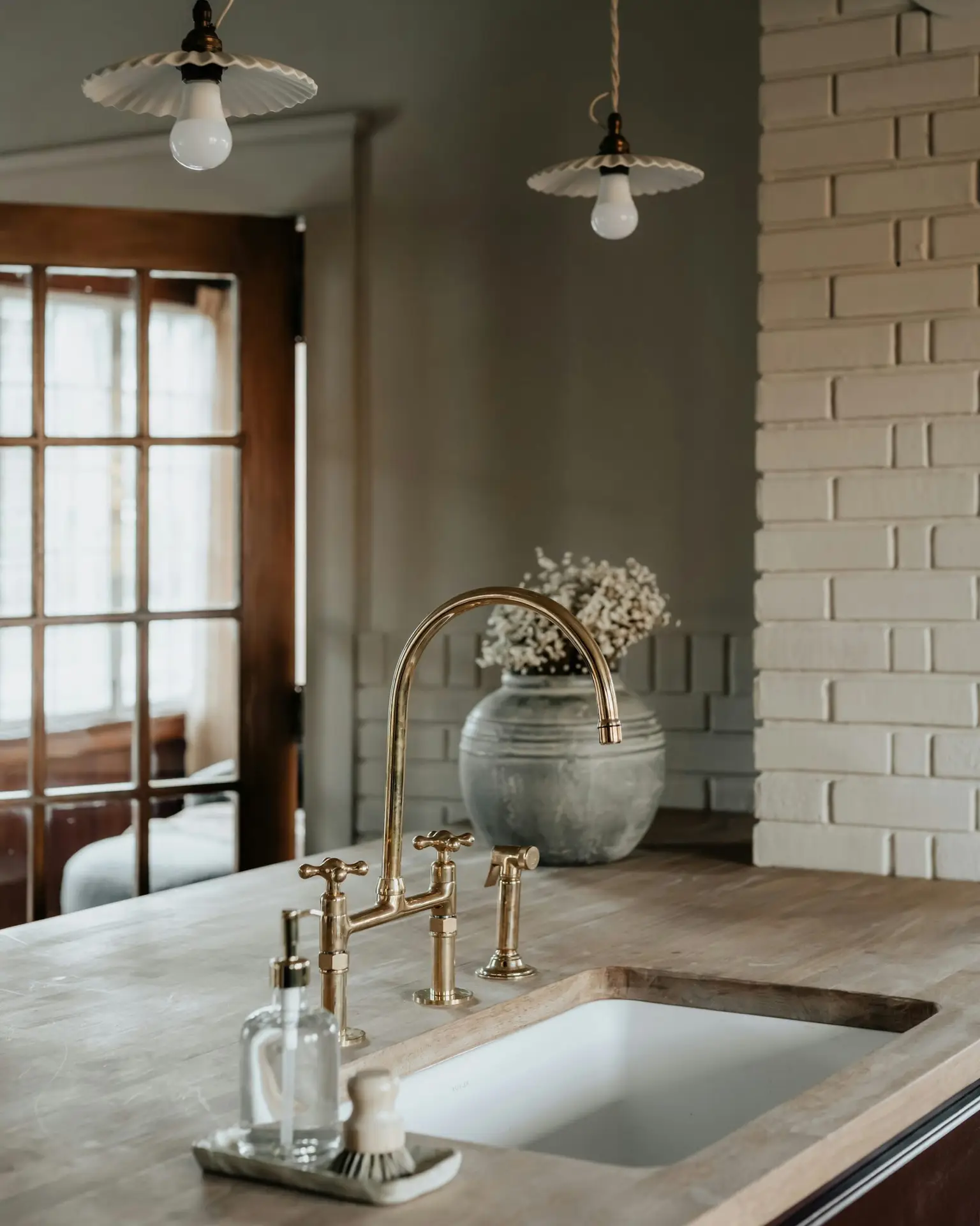 A brass bridge tap over a deep sink, with a stone vase of dried flowers by the window