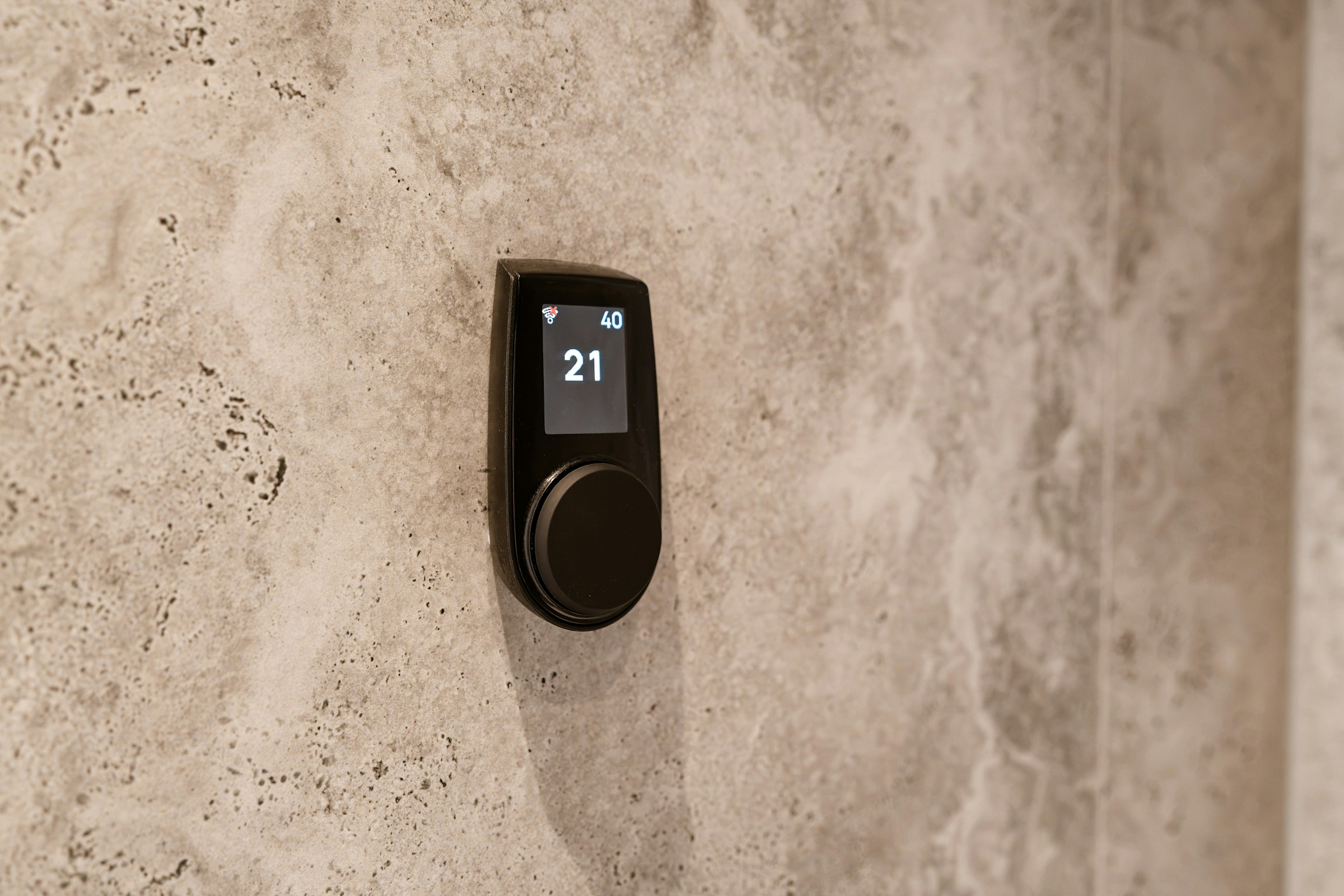 A slim black heating control set into a pale stone wall