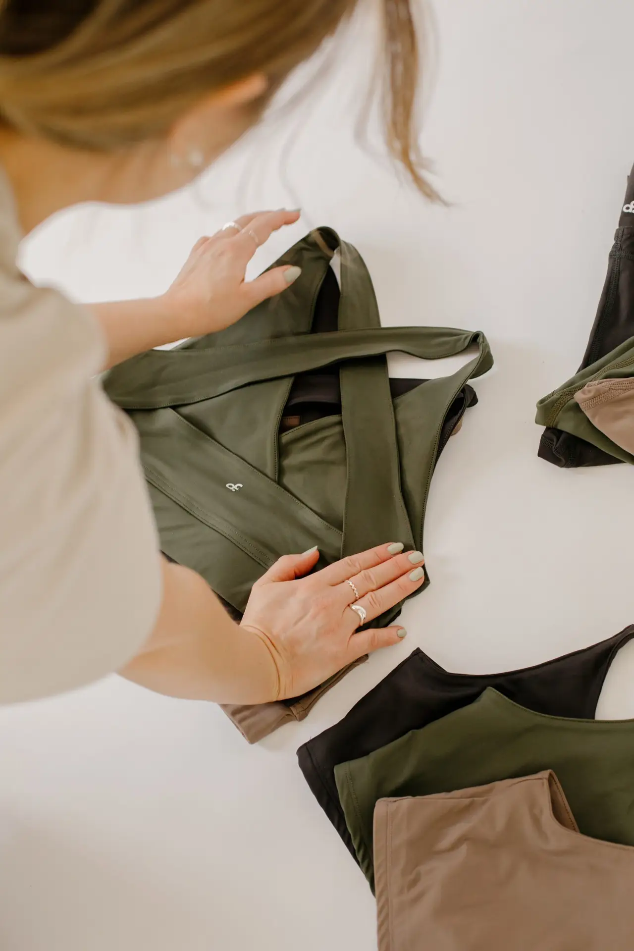 Hands arranging Actively Conscious activewear in olive and mocha on a white table