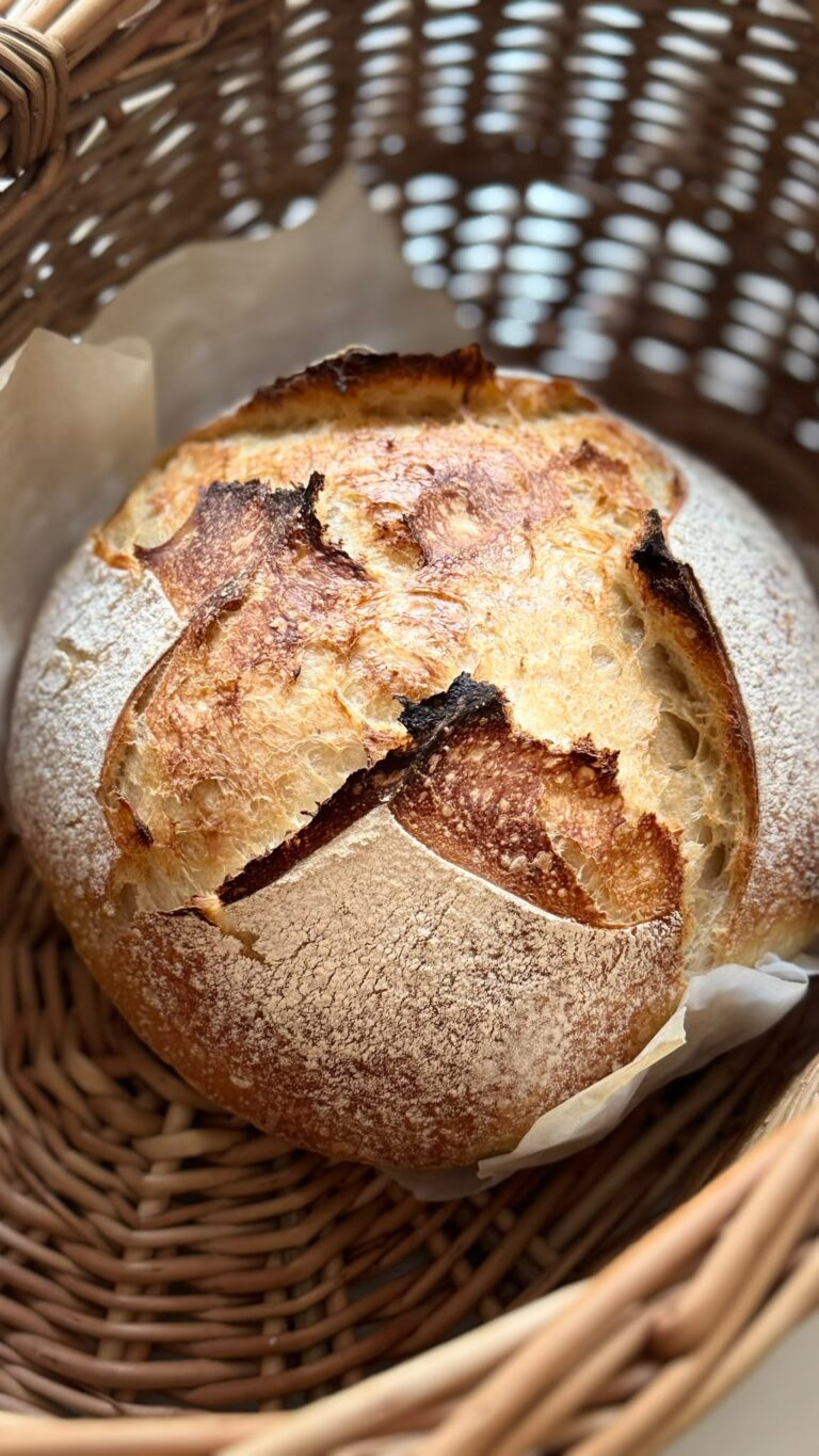 A freshly baked sourdough loaf in a woven basket