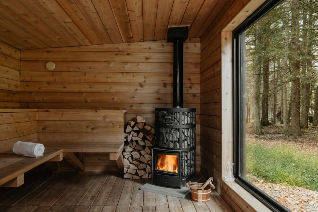A wood-lined sauna cabin with a stove and a window onto the forest