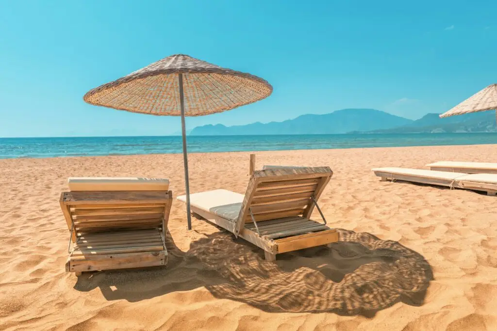 Two wooden sun loungers under a straw parasol on a quiet beach